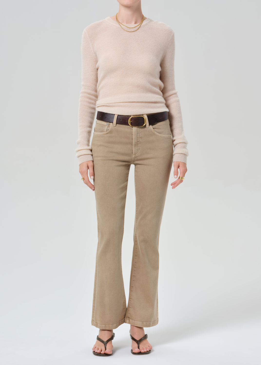 Person wearing a beige sweater and tan pants with a belt on a grey background