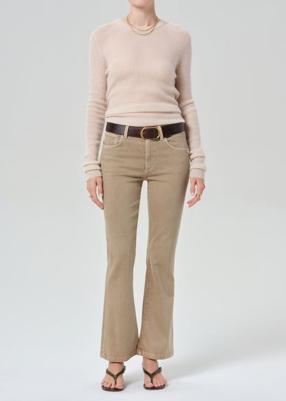Person wearing a beige sweater and tan pants with a belt on a grey background