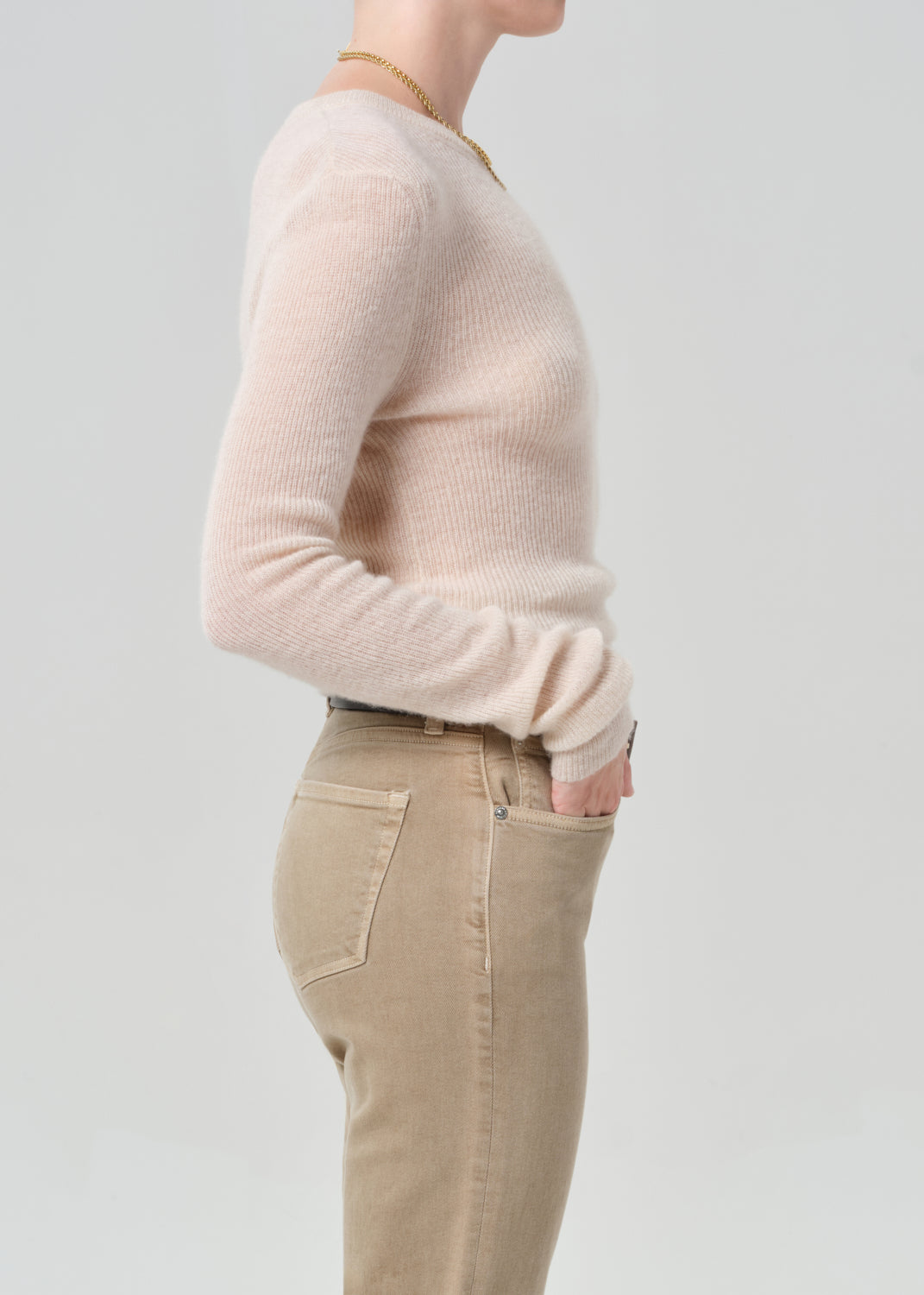 Person wearing a light cream sweater and beige pants on a plain background