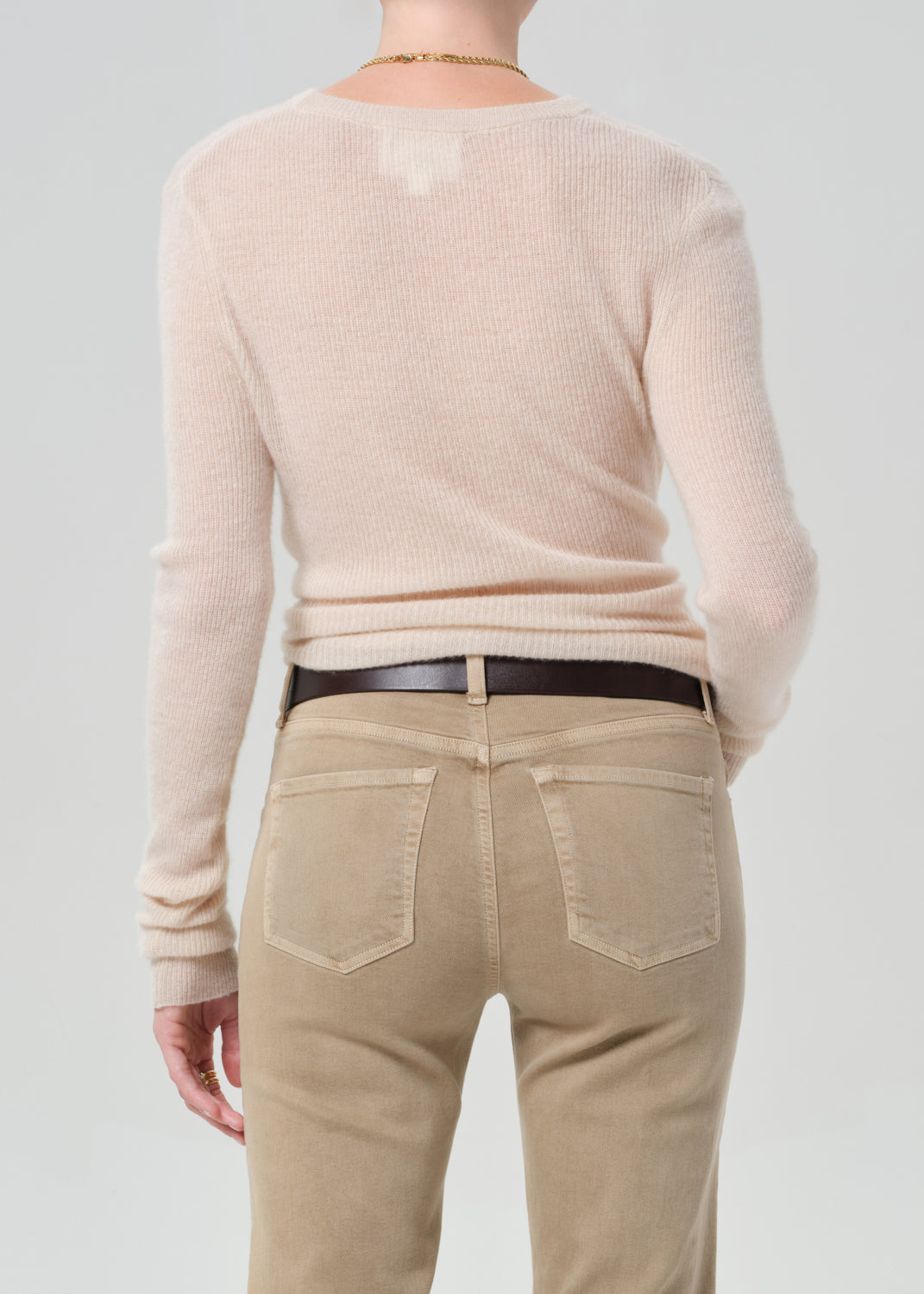 Person wearing a beige sweater and tan pants on a plain background