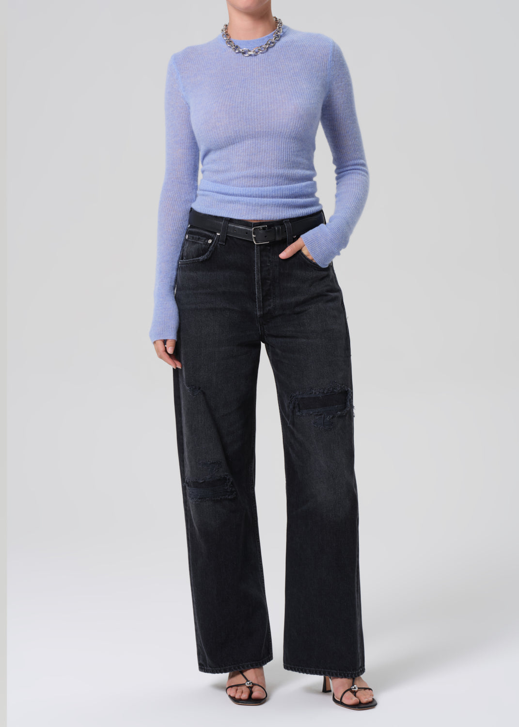 Person wearing a light blue sweater and black jeans on a white background