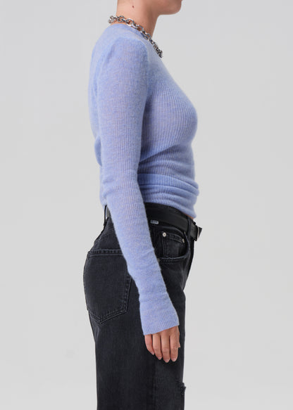 Person wearing a light blue sweater and black pants on a plain background
