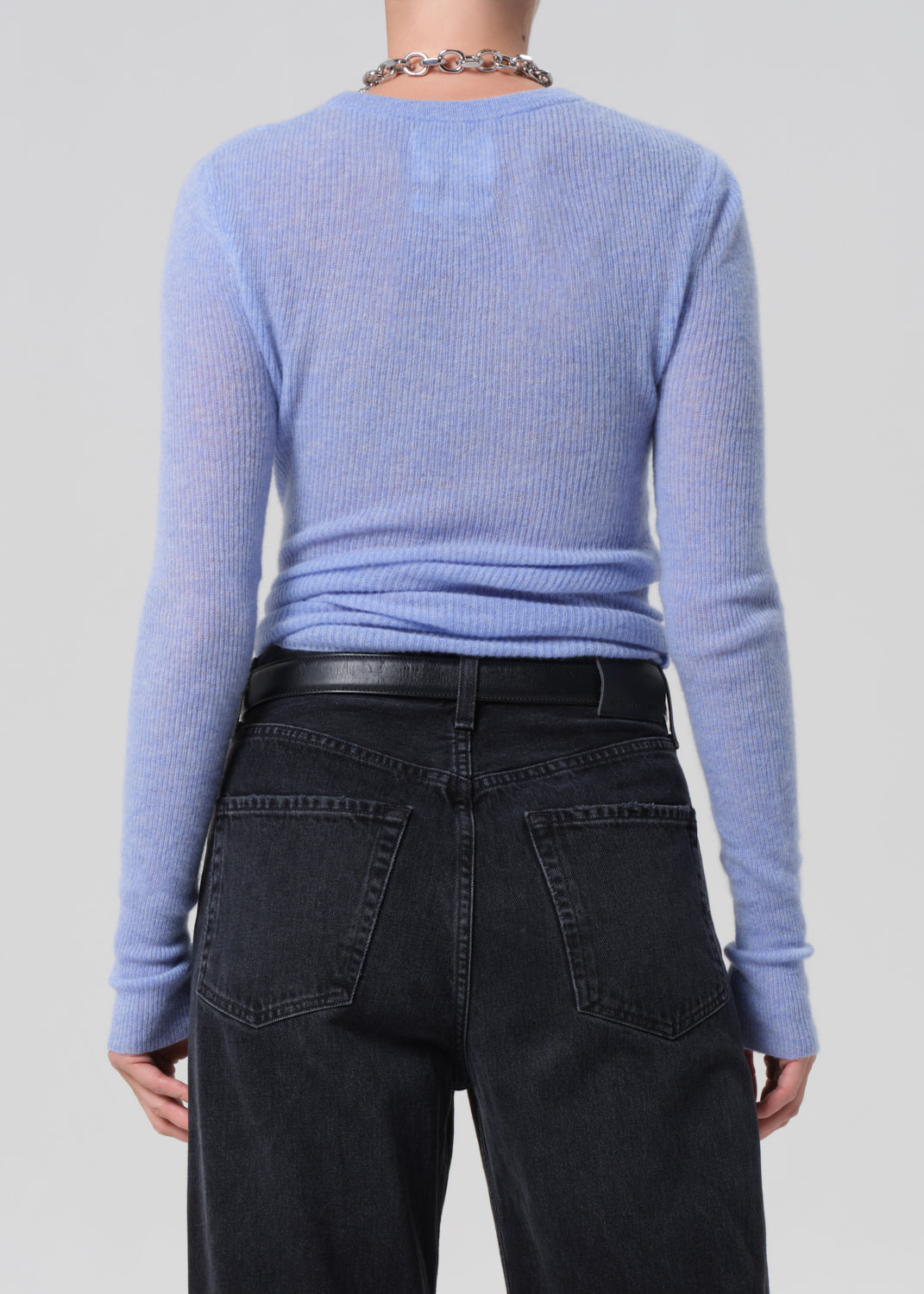 Person wearing a light blue sweater and dark jeans on a plain background