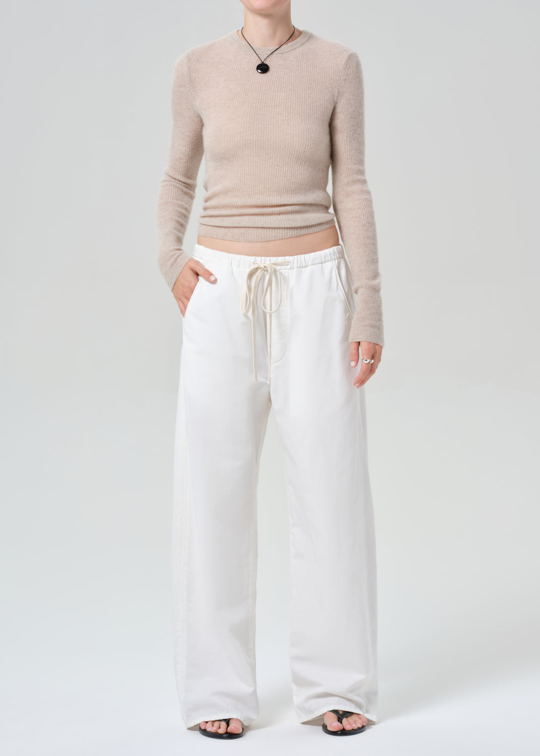 Person wearing a beige sweater and white pants on a plain background