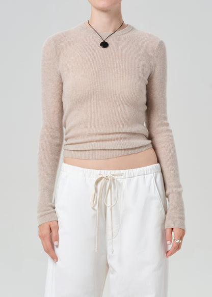 Person wearing a beige sweater and white pants on a plain background