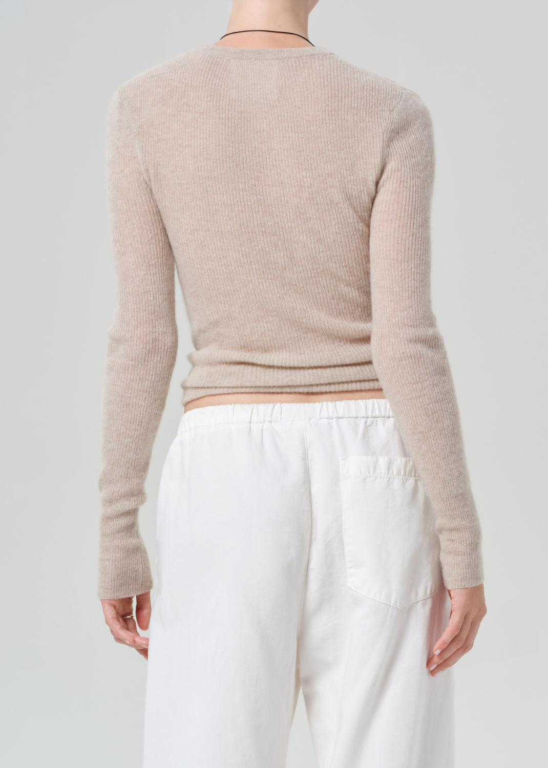 Person wearing a beige sweater and white pants on a plain background