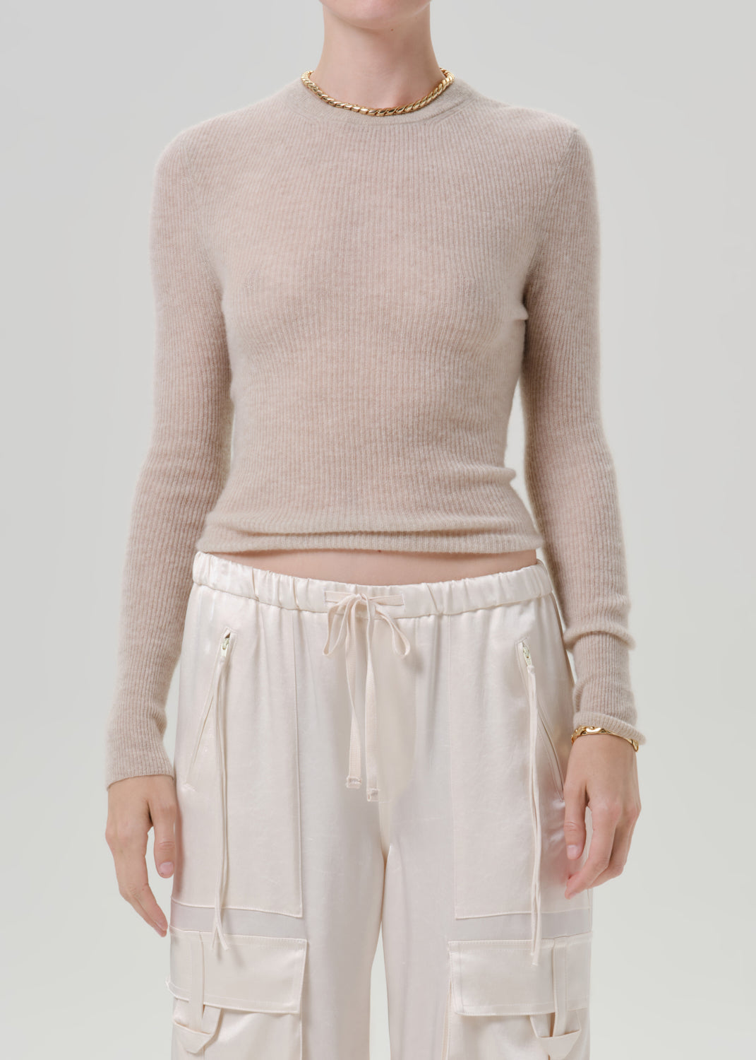 Person wearing a beige sweater and white pants on a grey background