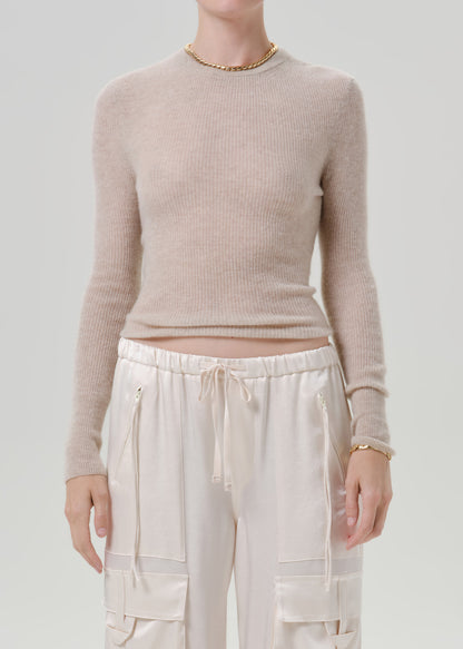 Person wearing a beige sweater and white pants on a grey background