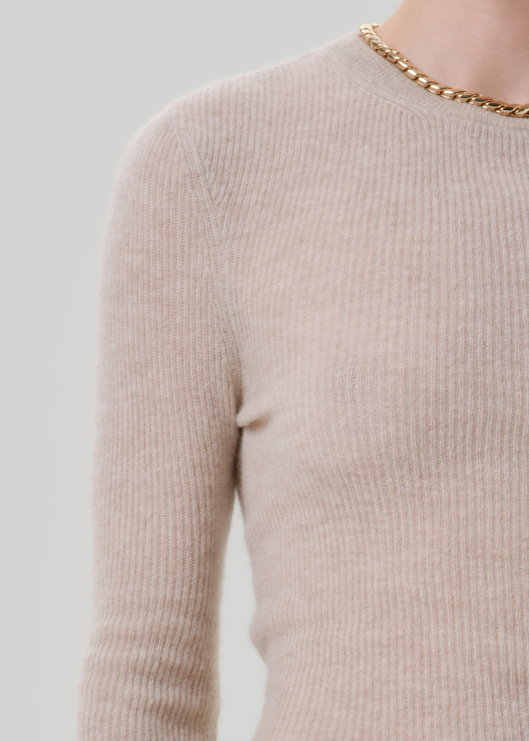 Close up shot of person wearing a beige sweater on a grey background