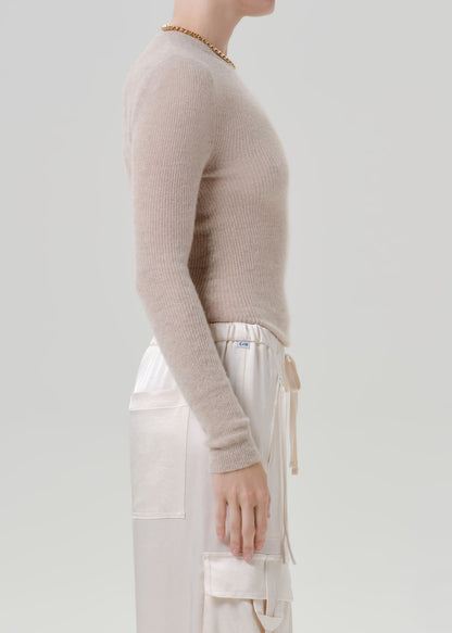 Person wearing a beige sweater and white pants on a grey background