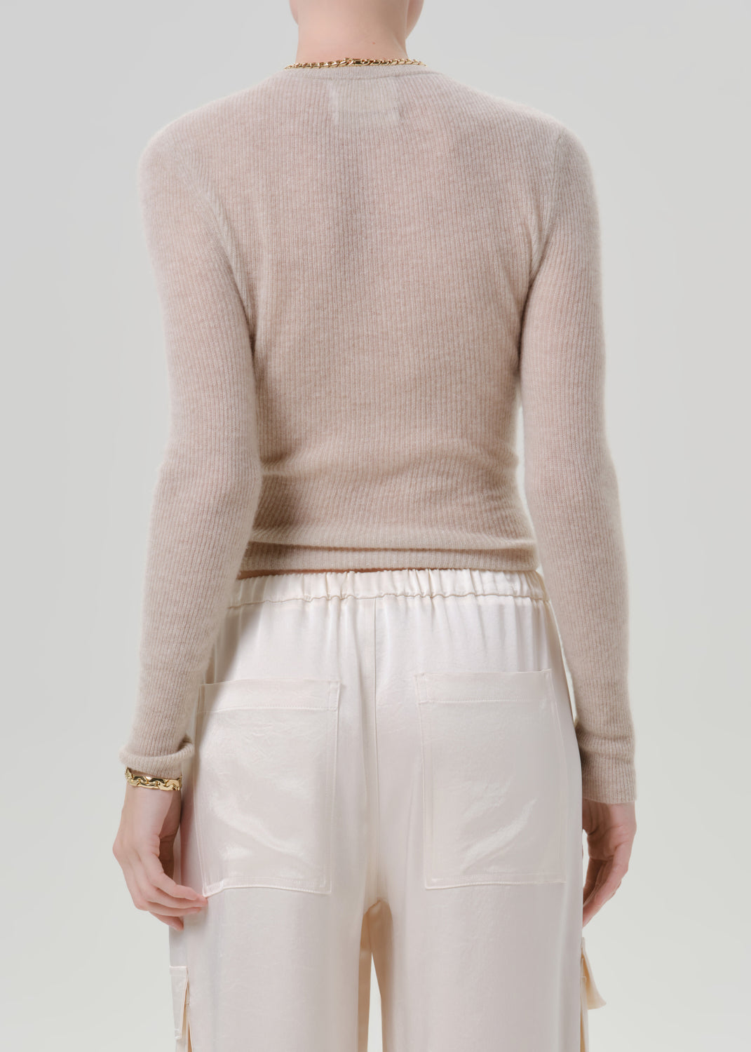 Person wearing a beige sweater and white pants on a grey background