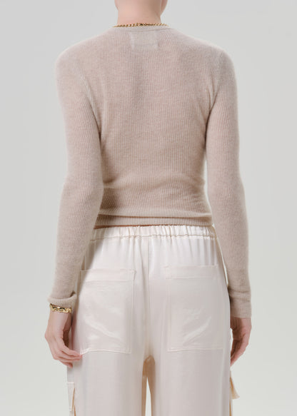 Person wearing a beige sweater and white pants on a grey background