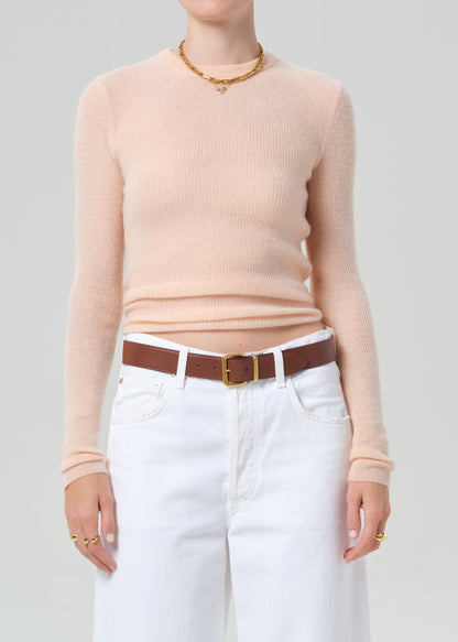 Person wearing a light peach sweater and white jeans with a brown belt on a plain background