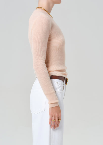 Person wearing a light peach sweater and white jeans with a brown belt on a plain background