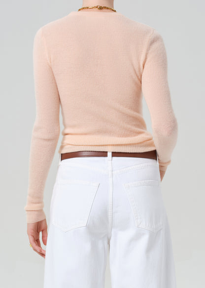 Person wearing a light peach sweater and white jeans with a brown belt on a plain background