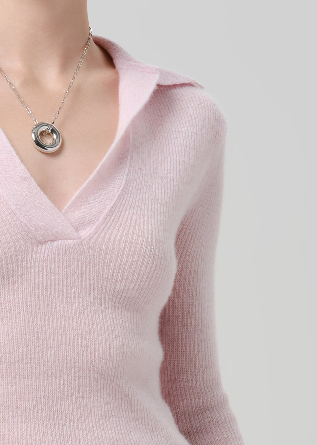 Person wearing a light pink ribbed knit polo sweater on a grey background