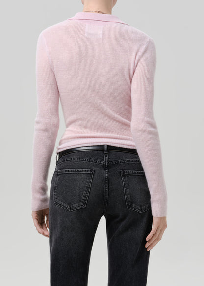 Person wearing a light pink ribbed knit polo sweater with black jeans viewed from the back on a grey background