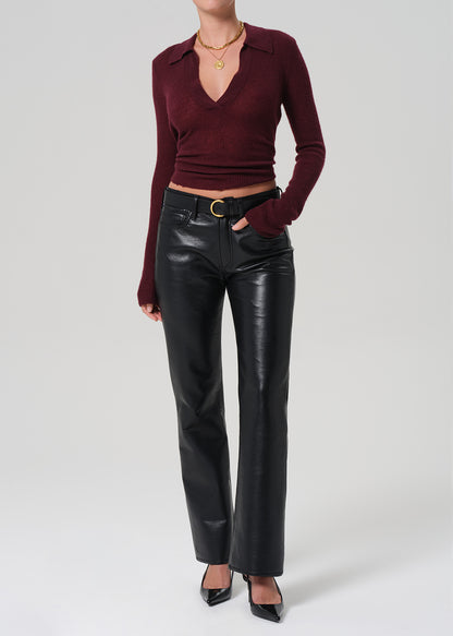 Person wearing a burgundy polo sweater and black leather pants on a light gray background