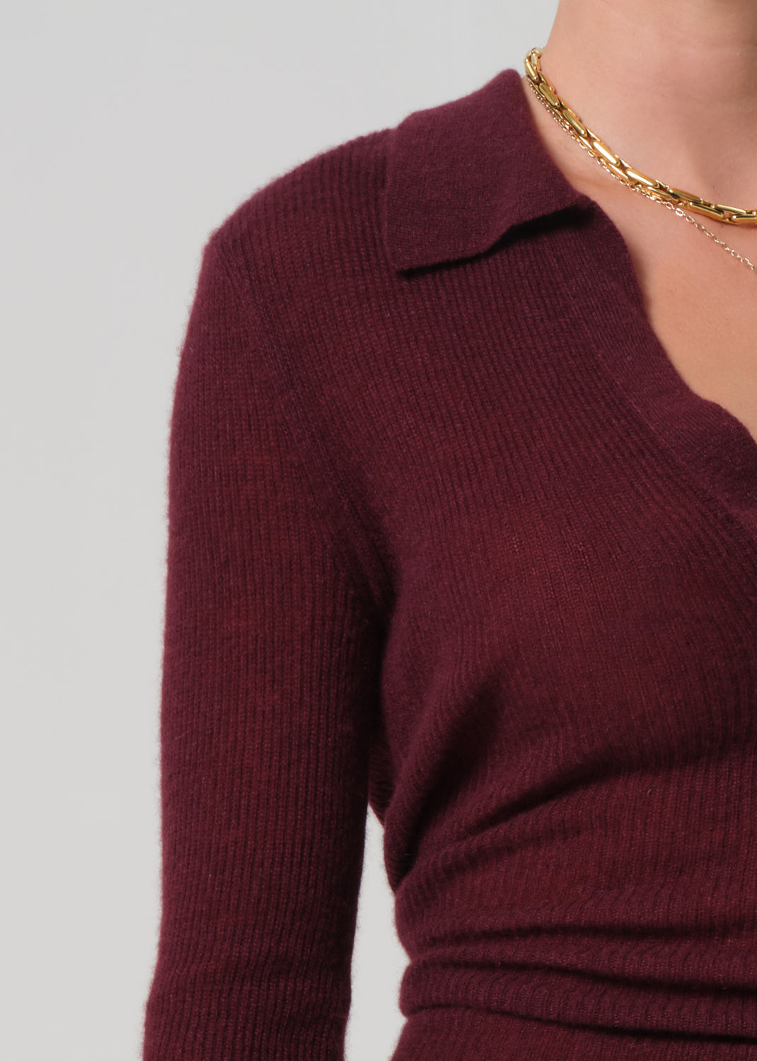 Person wearing a burgundy polo sweater and black leather pants on a light gray background