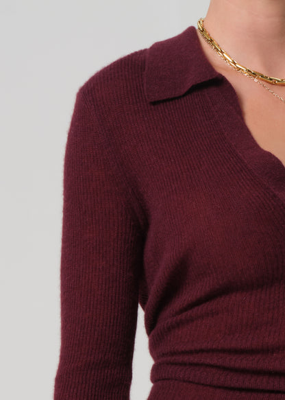 Person wearing a burgundy polo sweater and black leather pants on a light gray background