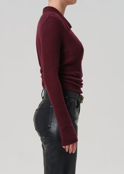 Person wearing a burgundy polo sweater and black leather pants on a light gray background