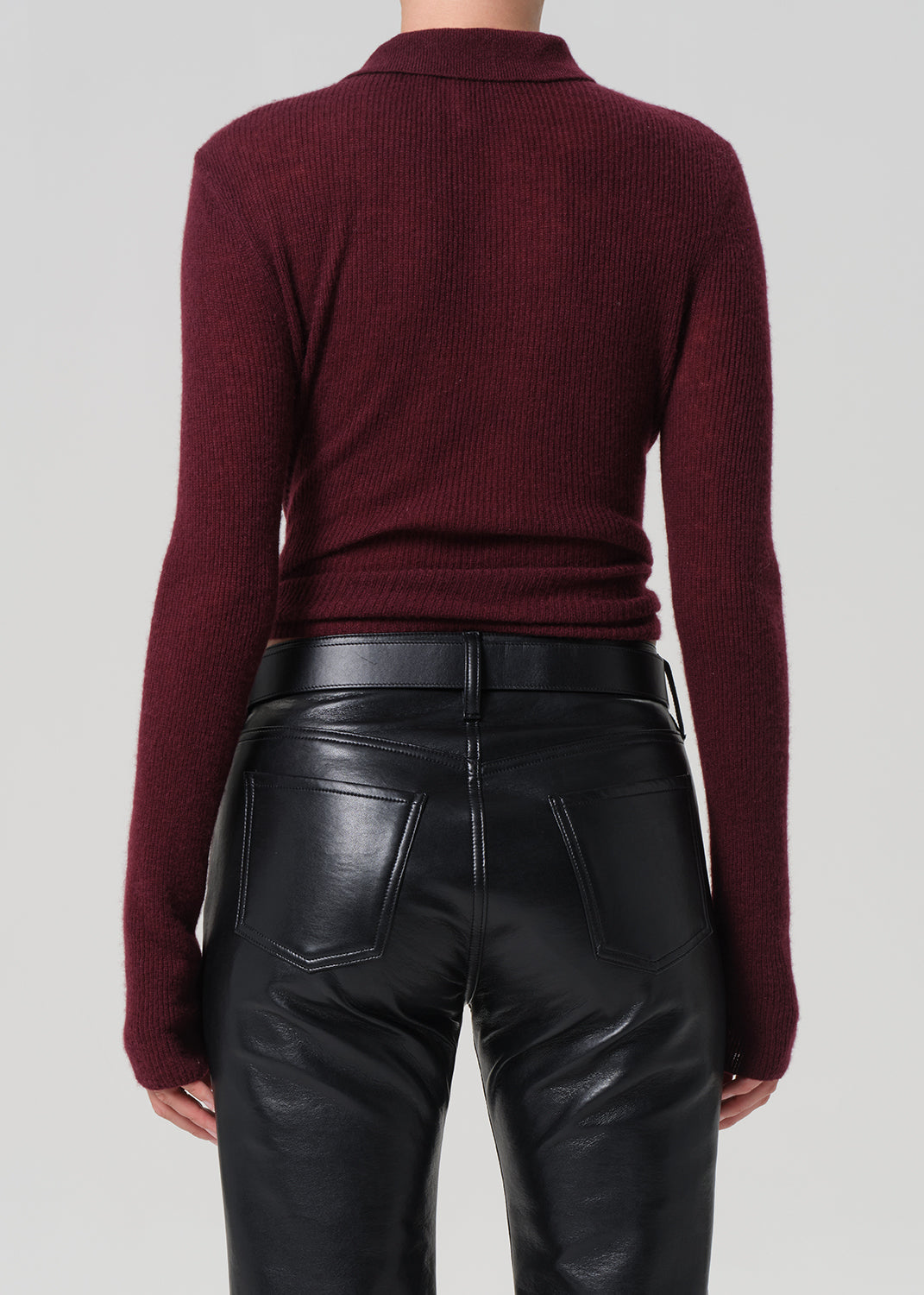 Person wearing a burgundy polo sweater and black leather pants on a light gray background