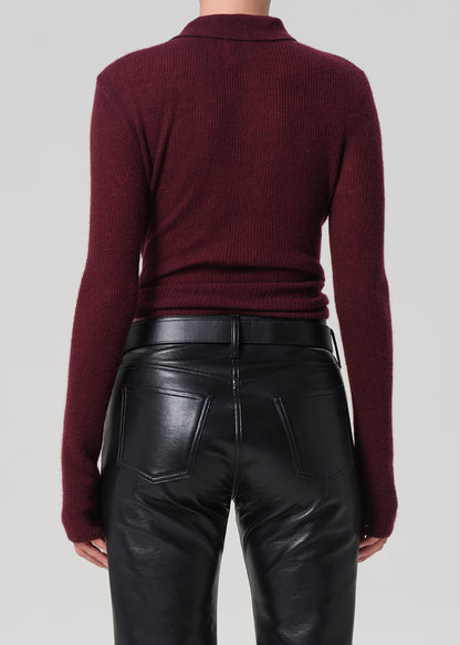 Person wearing a burgundy polo sweater and black leather pants on a light gray background