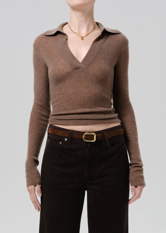 A model wearing a brown ribbed knit polo-collar sweater tucked into dark brown corduroy trousers with a brown belt and gold buckle, against a grey background.