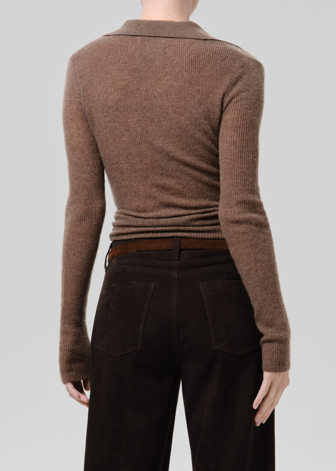 A model shown from the back wearing a brown ribbed knit long-sleeve top and dark brown wide-leg trousers, photographed against a grey background.