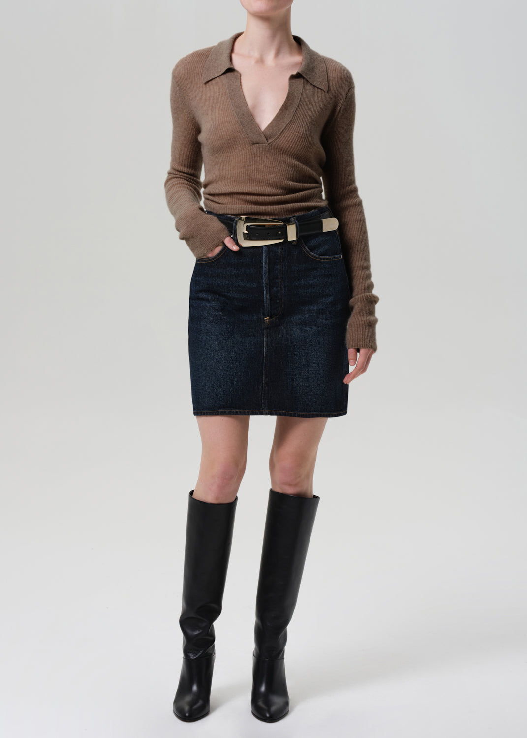 Person wearing a brown sweater, black skirt, and black knee-high boots on a white background