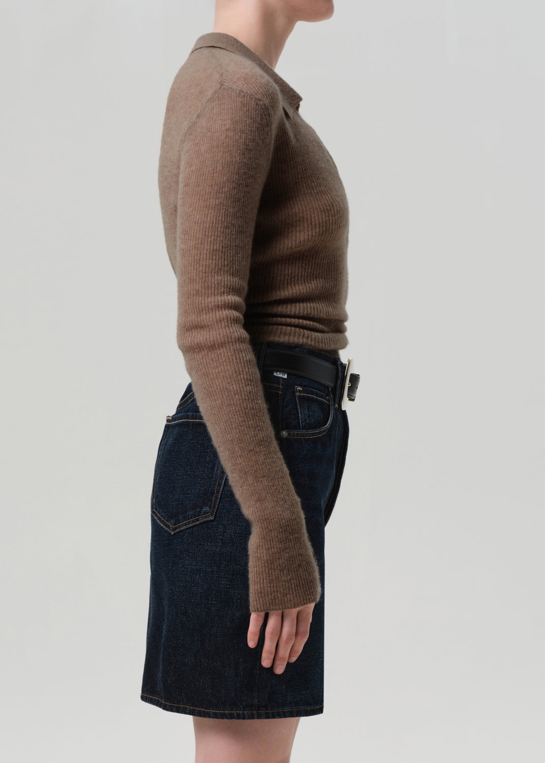 Person wearing a brown sweater and dark denim skirt on a light gray background