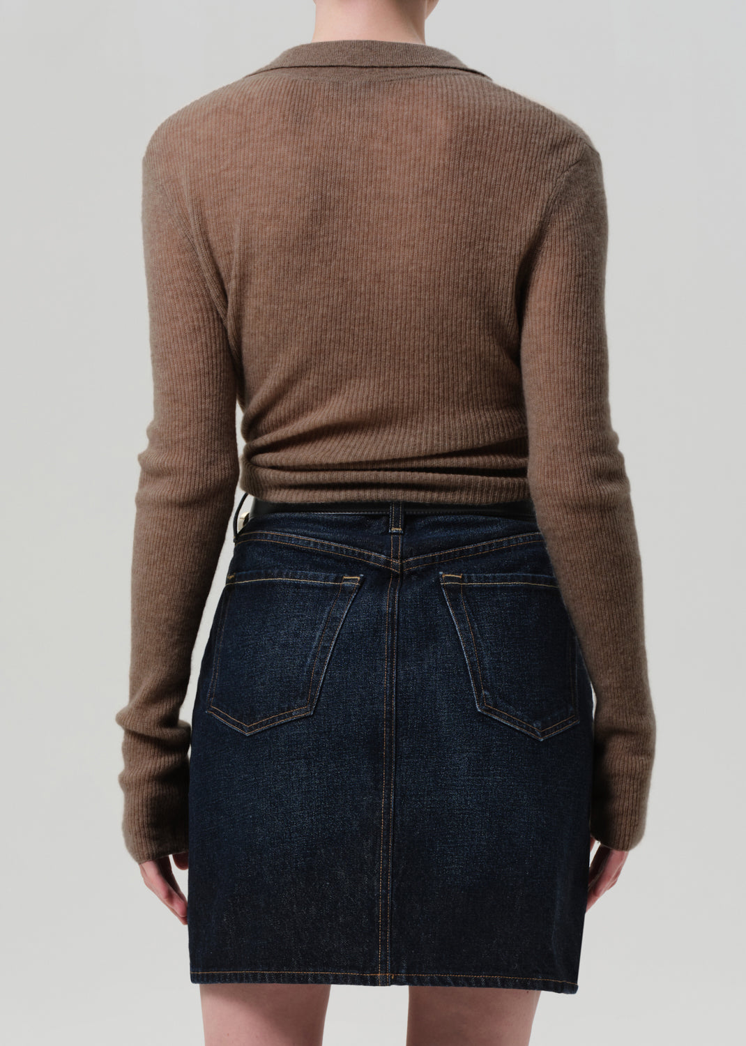 Person wearing a brown sweater and dark denim skirt on a plain background