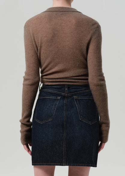 Person wearing a brown sweater and dark denim skirt on a plain background