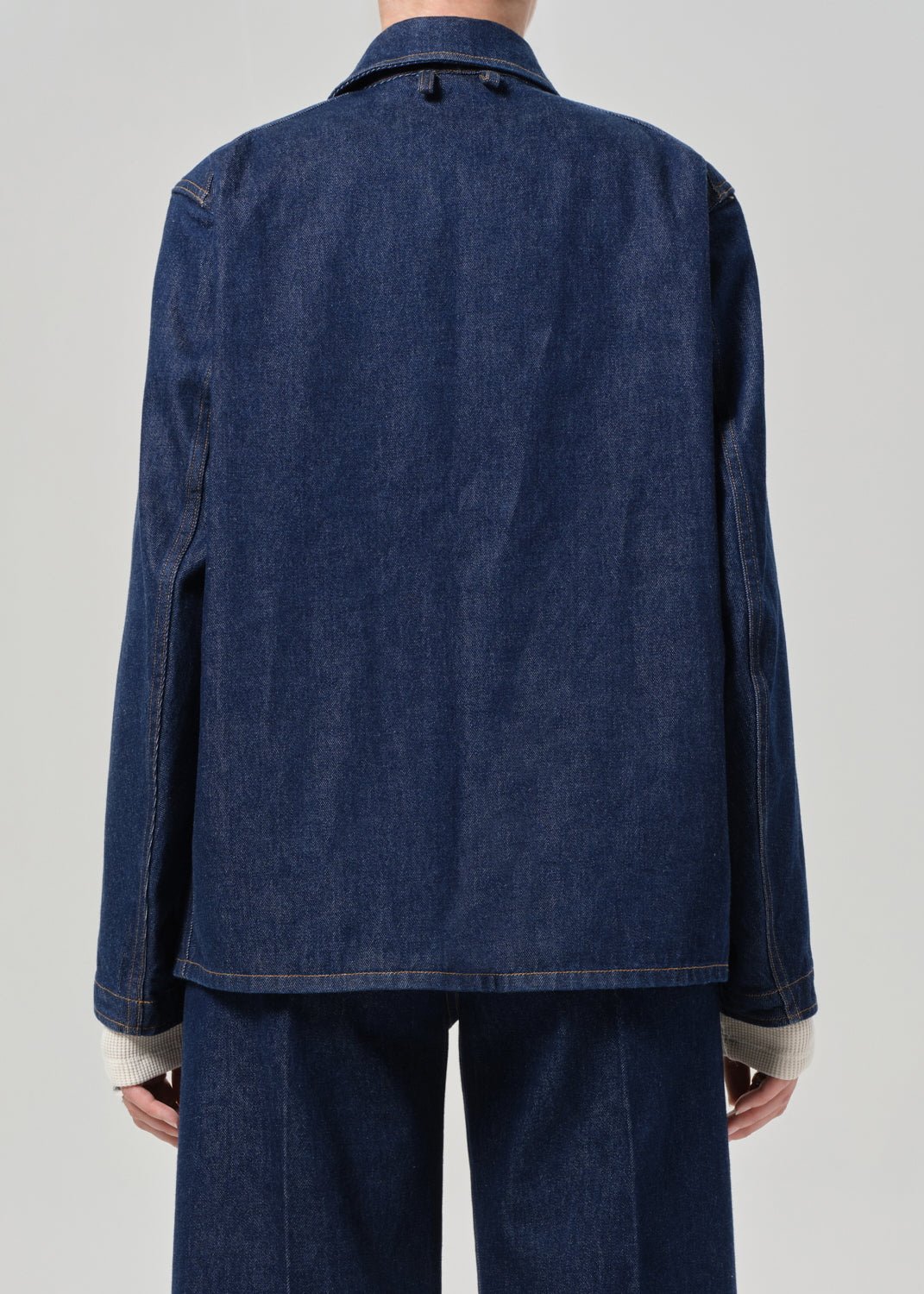 Person wearing a blue denim jacket and pants on a gray background