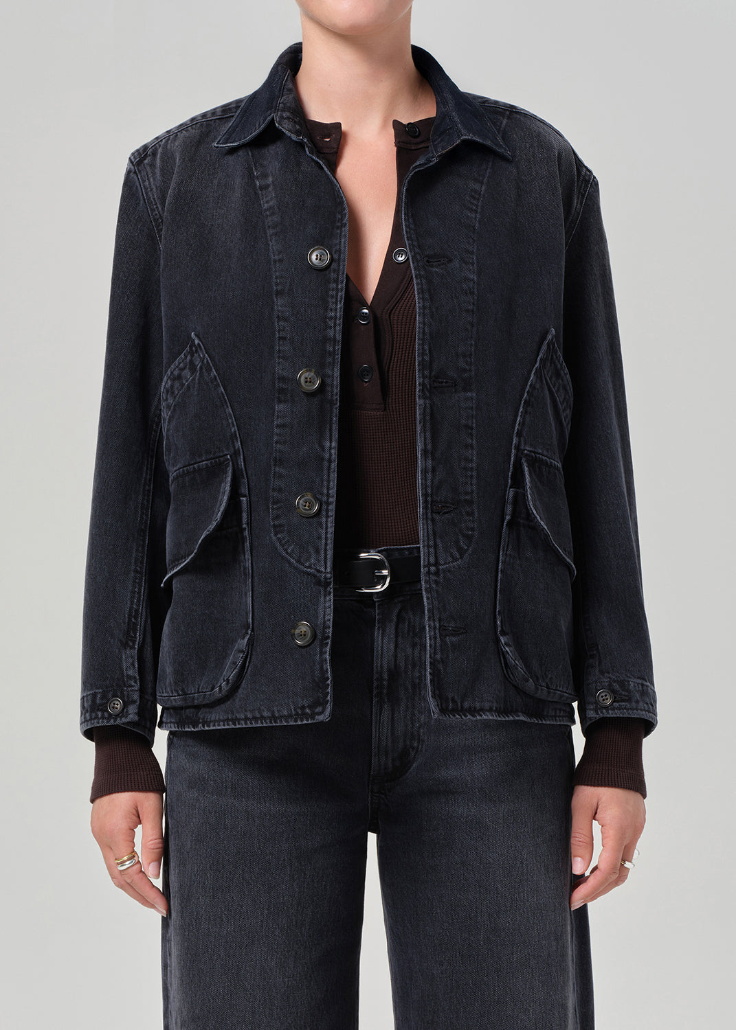 Person wearing a black denim jacket on a gray background