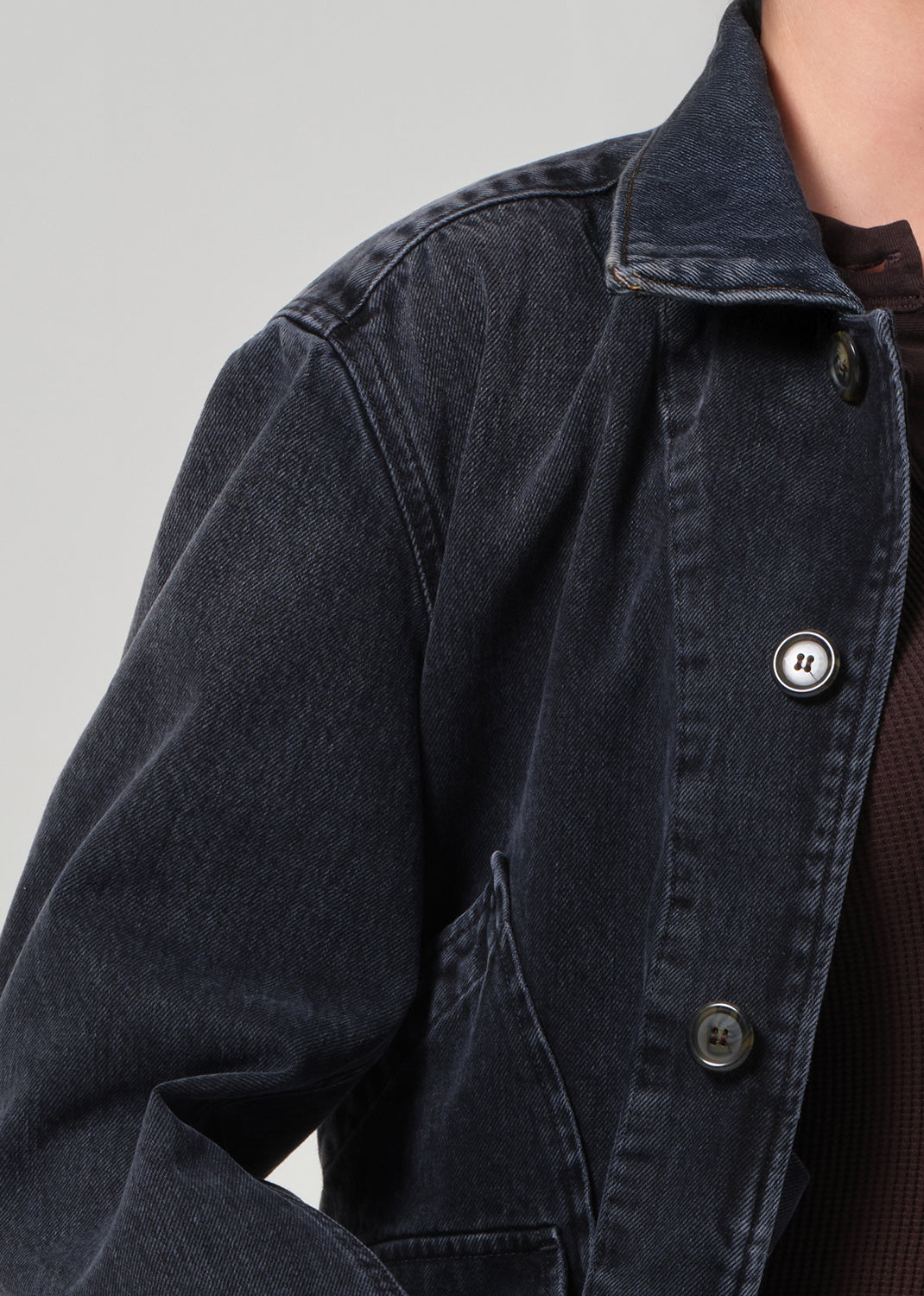 Close-up of a dark denim jacket with buttons on a plain background