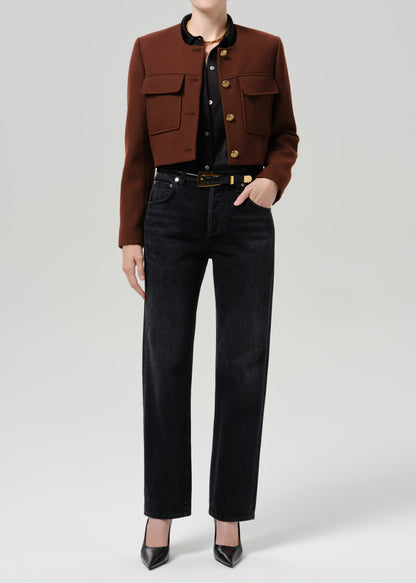 Person wearing a brown tailored cropped jacket with black straight leg jeans on a grey background