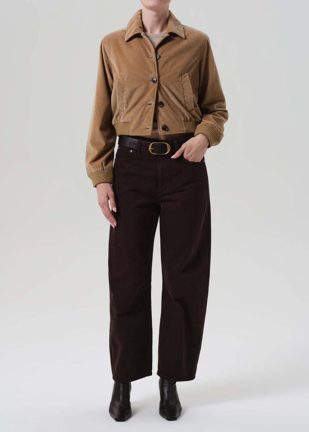 Person wearing a brown jacket and dark pants on a white background