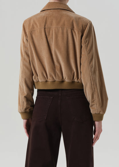 Person wearing a brown corduroy jacket and dark pants on a plain background