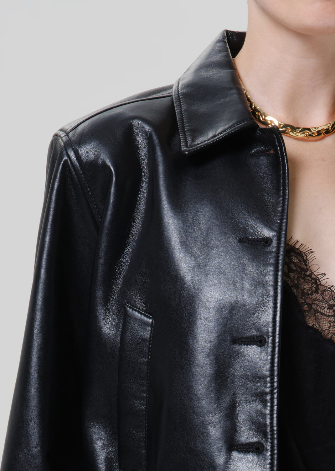 Close-up of a black leather button-up shirt on a grey background.