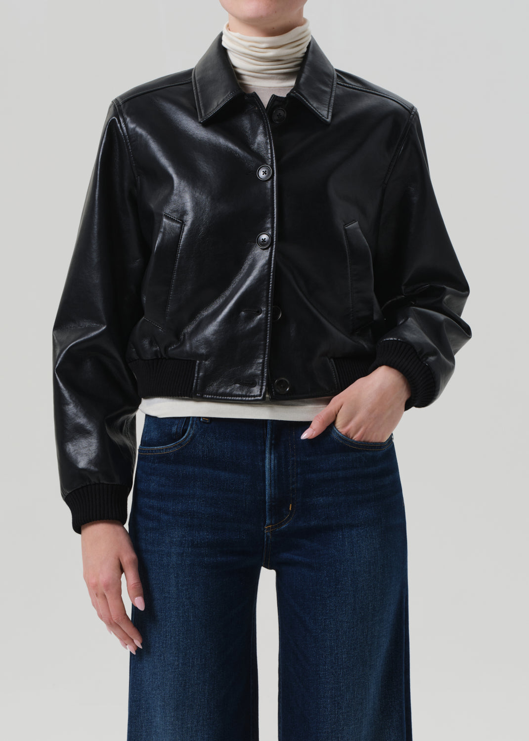 Person wearing a black leather jacket and blue jeans on a plain background