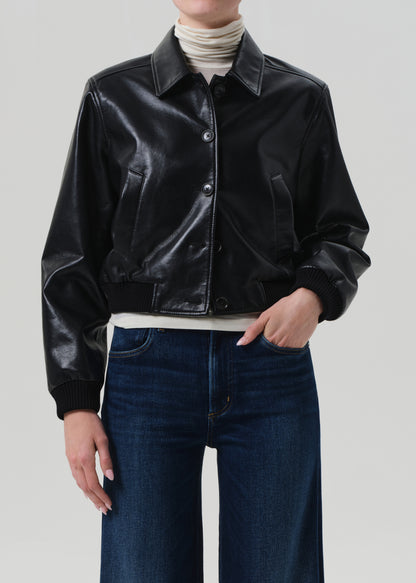 Person wearing a black leather jacket and blue jeans on a plain background