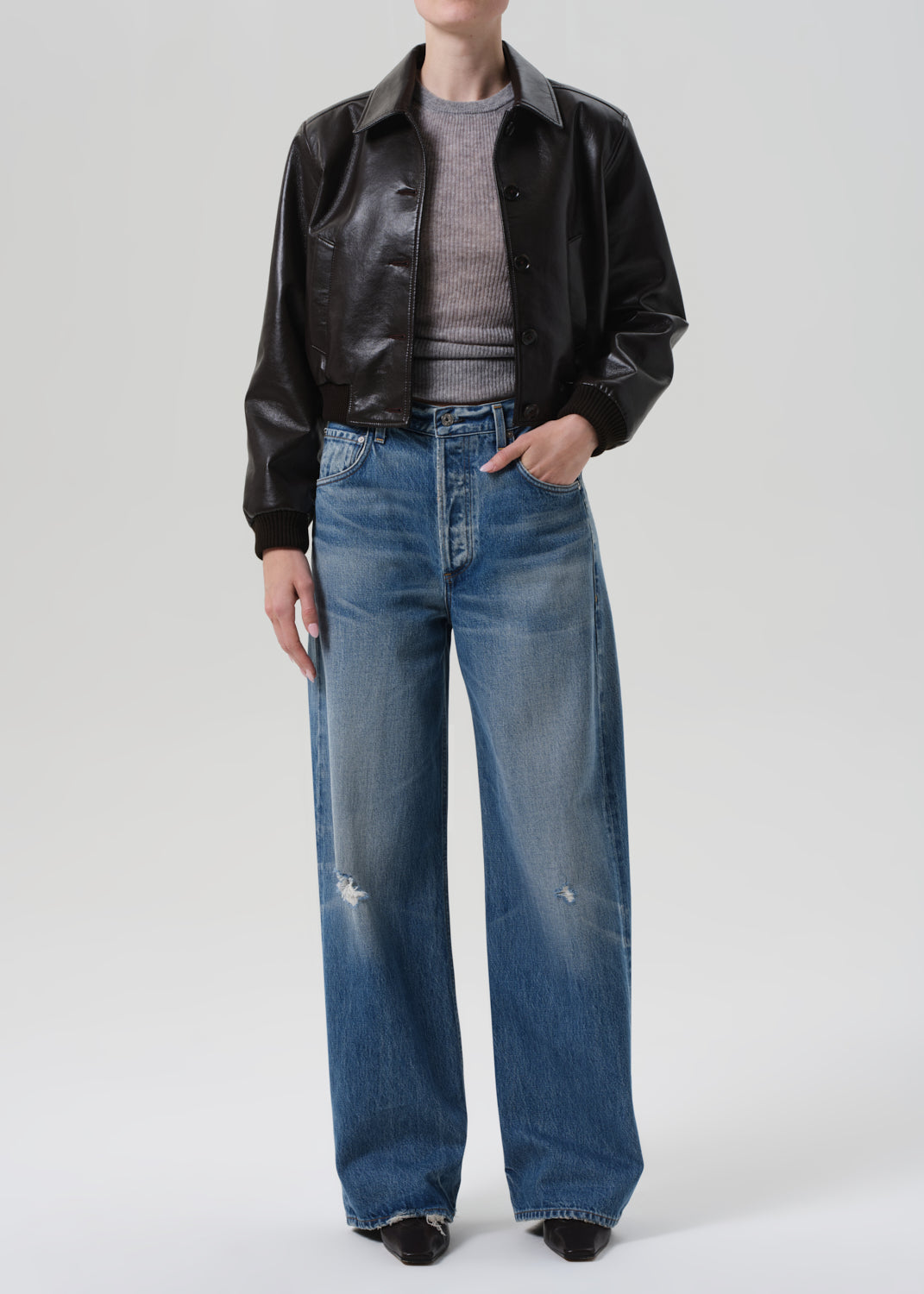 Person wearing a brown leather jacket and blue jeans on a white background