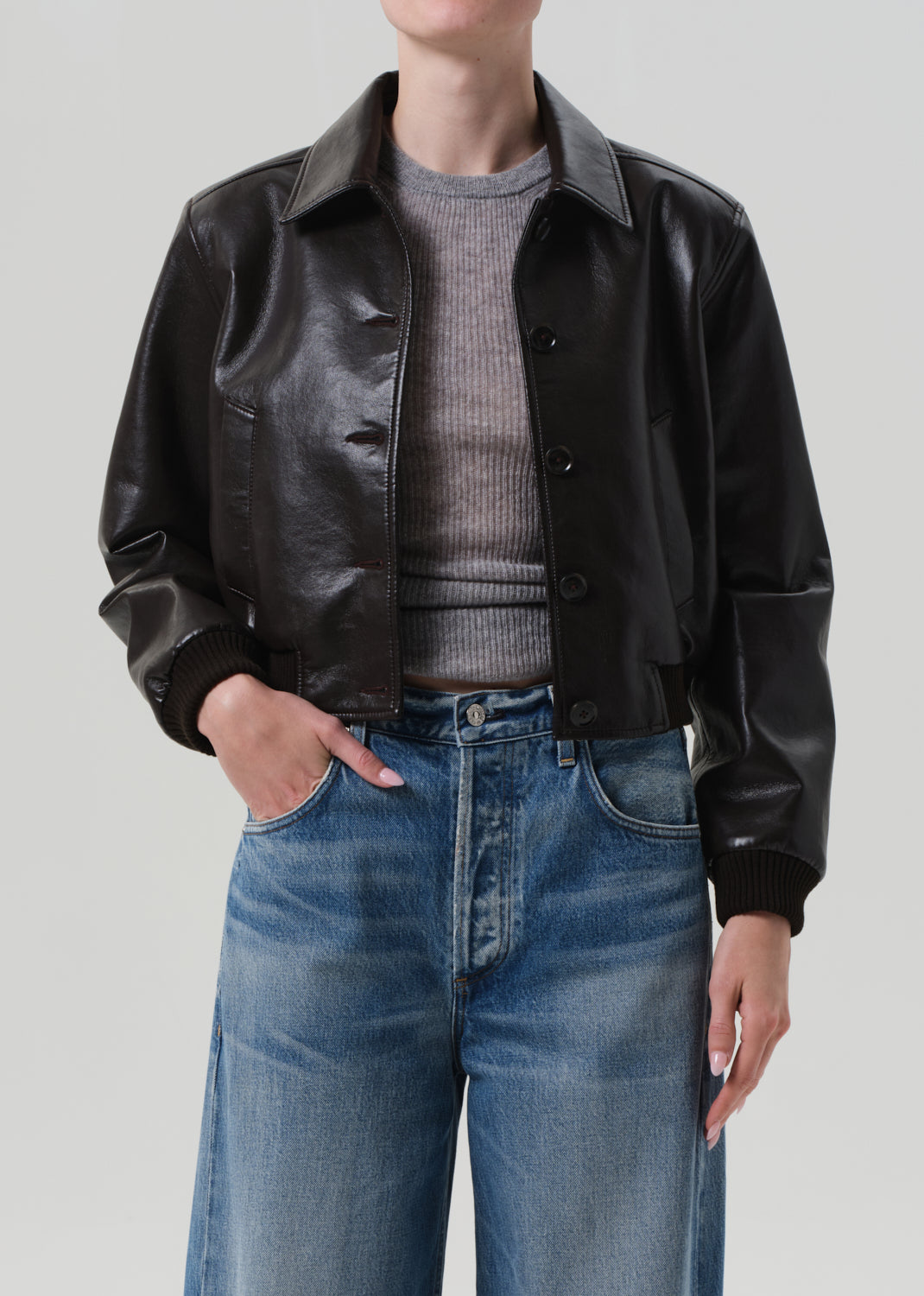 Person wearing a brown leather jacket and blue jeans on a plain background