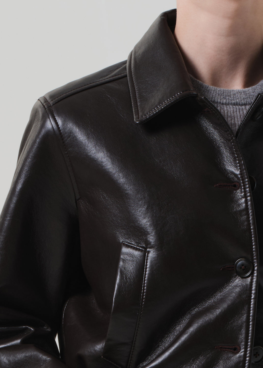 Close-up of a brown leather jacket worn by a person on a light gray background