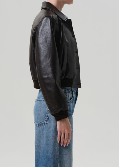 Person wearing a brown leather jacket and blue jeans on a light gray background