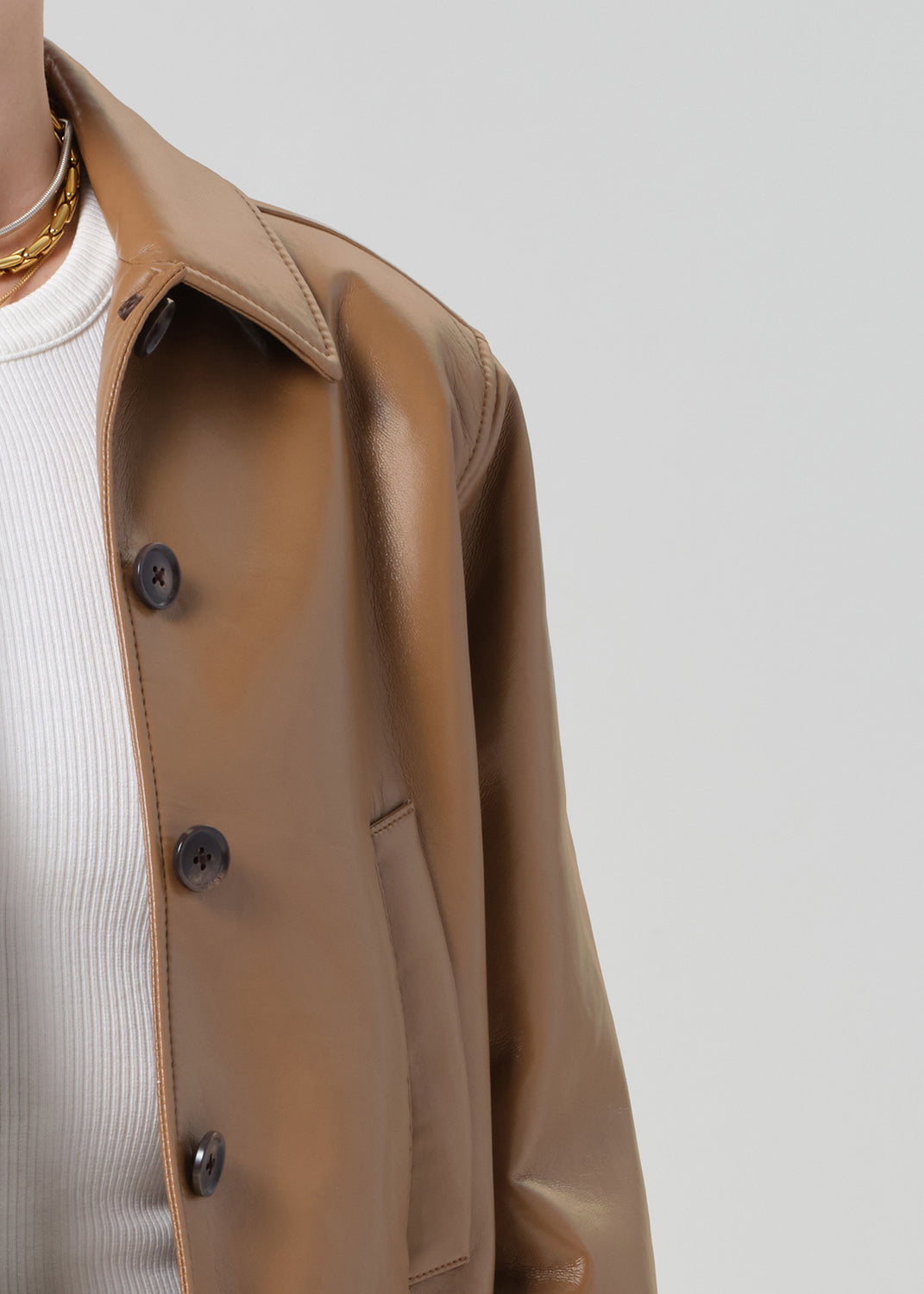 Person wearing a brown leather jacket and blue jeans shorts on a plain background