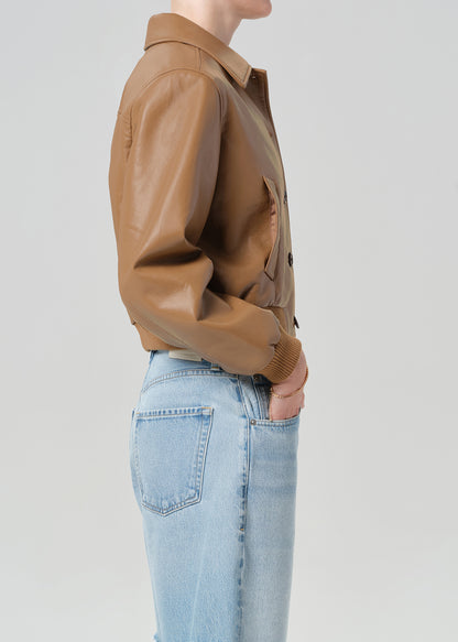 Person wearing a brown leather jacket and blue jeans shorts on a plain background