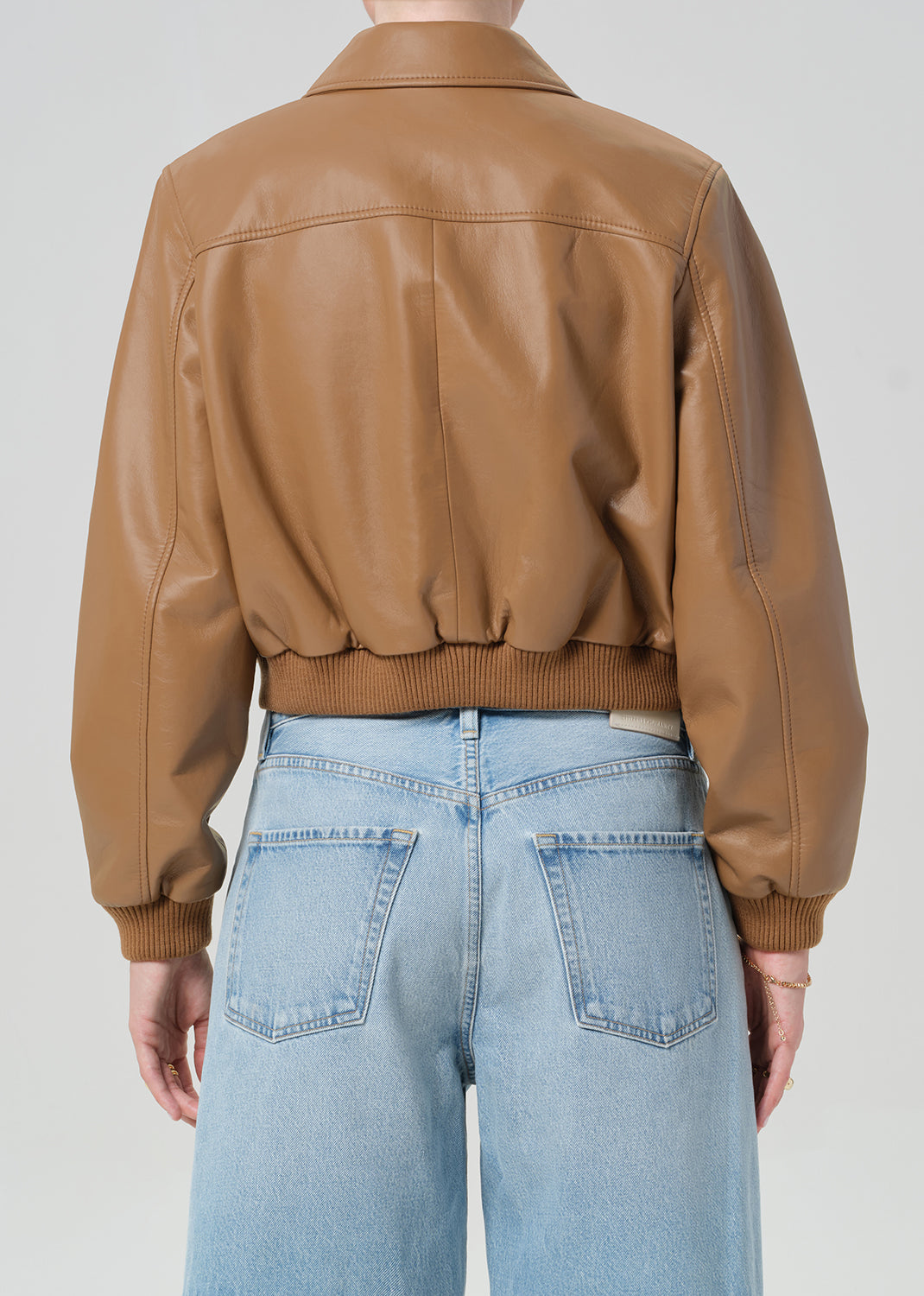 Person wearing a brown leather jacket and blue jeans shorts on a plain background