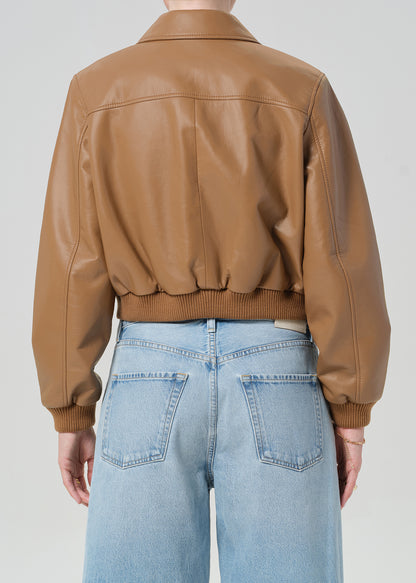 Person wearing a brown leather jacket and blue jeans shorts on a plain background